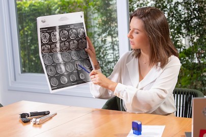 Dra. Lorena Raulik Cyrino em atendimento explicando uma radiografia. Ela está sentadaem frente à mesa, onde há um bloco de receitas, um carimbo e utensílios médicos.